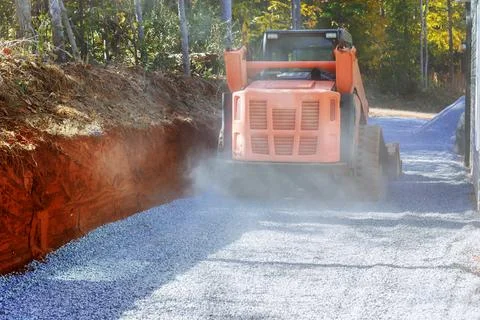 Using tractor to lay crushed stone gravel fill on top surface of new road as a Foto stock