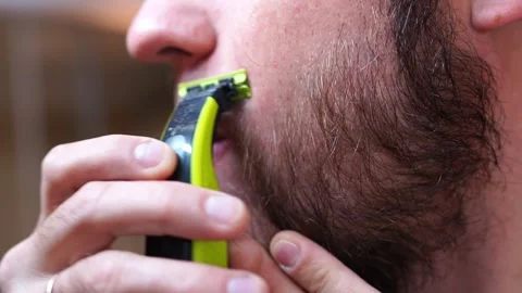 Using a trimmer, the man grooms his beard with a thumb gesture Stock Footage 287562408