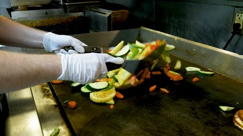 Using two spatulas to fry vegetables on large grill Stockbeeldmateriaal 94276412