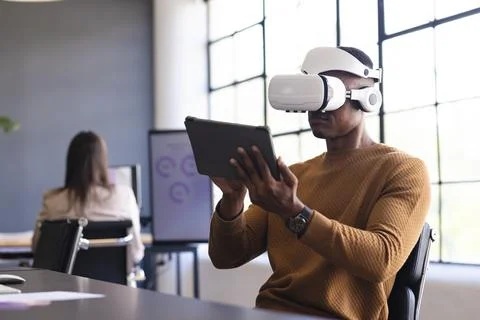 Using VR headset and holding tablet, man working in modern office setting Fotos Stock