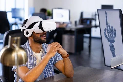 Using VR headset, Indian man interacting with robotic hand design on computer Stock-Fotos