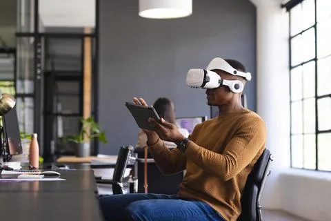 Using VR headset, man interacting with tablet in modern office workspace Stock Photos