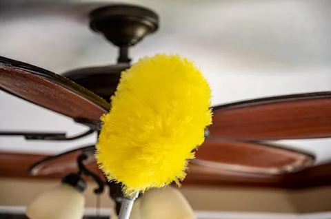 Using a wand feather duster to remove and clean dust from a ceiling fan Stock Photos