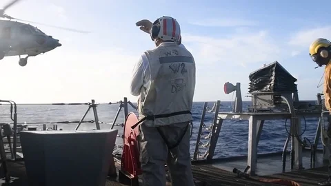 USS Curtis Wilbur flight deck crew signalling to MH-60 Seahawk helicopter pilot Stock Footage 104855700