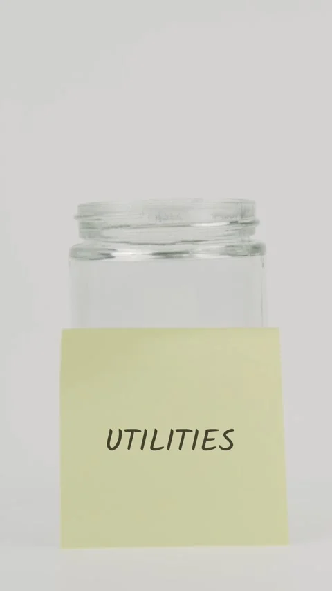 Utilities text or word on yellow sticky note attached to glass jar with hand Stock Footage 311801592