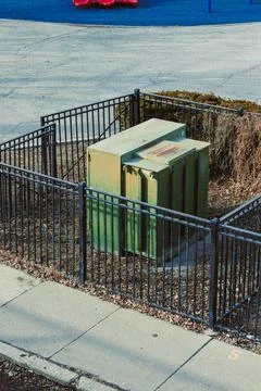 A utility box sits inside a black fence at a city park playground. The ground Foto stock