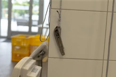 Utility knife hanging from tiled wall with rope loop and blurred background Stock-Fotos