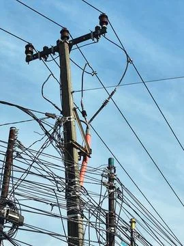 Utility pole is crowded with a web of black wires against a bright blue sky c Фото