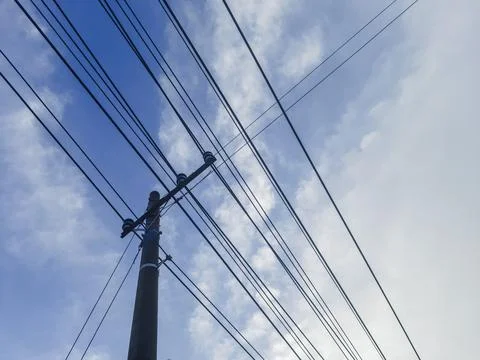 Utility pole supporting multiple dark electrical wires against bright blue sky Stock Photos