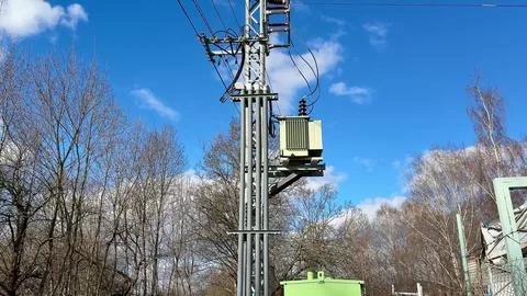 A utility pole supporting a transformer stands tall against a vibrant blue .. Stock Photos