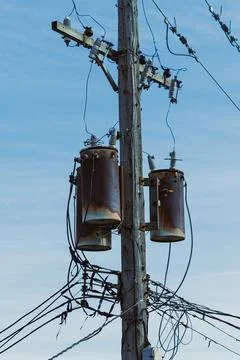 Utility poles support power transformers with wires and cables against a bl.. Stock Photos