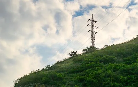 Utility tower rises over lush hillside under cloudy sky Stock Photos