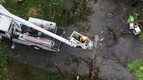 Utility worker in bucket repairs power lines near branch littered driveway in Stock Footage 340971155