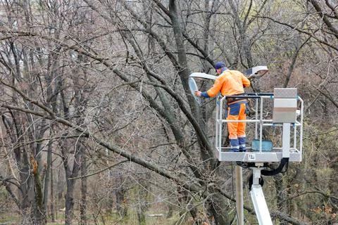 A utility worker changes a light bulb on a street lighting pole against the b Stock Photos