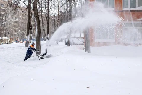 A utility worker cleans a path with a machine-driven snowplow during a snowfall. Stock Photos