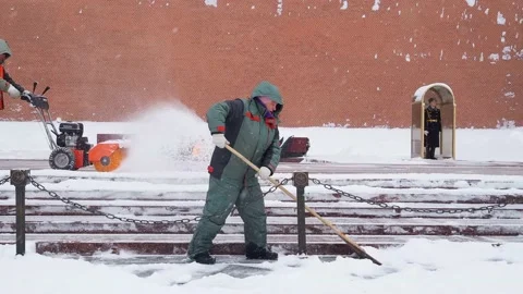 A utility worker cleans snow next to a soldier at a post near the Kremlin wall. Stock Footage 162315504