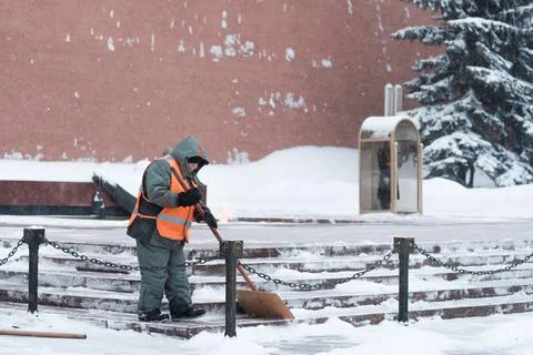 A utility worker cleans snow next to a soldier at a post near the Kremlin wall. Stock Photos