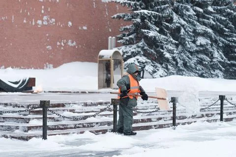 A utility worker cleans snow next to a soldier at a post near the Kremlin wall. Stock Photos