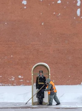 A utility worker cleans snow next to a soldier at a post near the Kremlin wall. Stock Photos