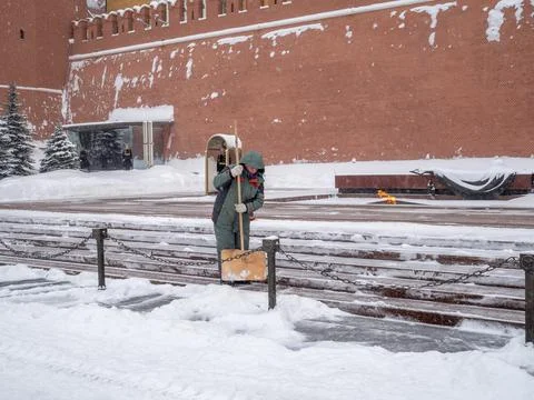 A utility worker cleans snow next to a soldier at a post near the Kremlin wal Stock Photos
