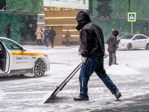 A utility worker removes snow with a scraper on a city street Stock Photos