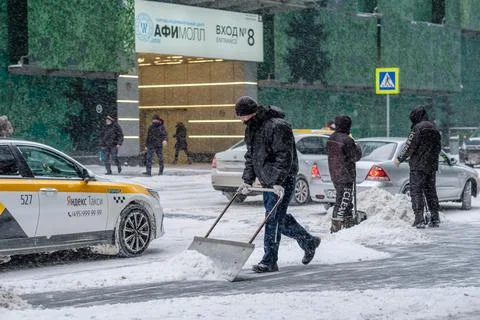 A utility worker removes snow with a scraper on a city street Stock Photos