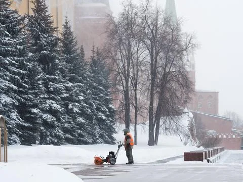 A utility worker uses a snowplow to remove snow from the walls of the Kremlin Stock Photos