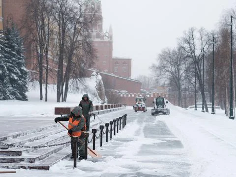 Utility workers and tractors remove snow from the Kremlin wall during a snowfall Stock Photos