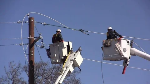 Utility Workers in cherry pickers -one hooks up to power pole Stock Footage 105138562