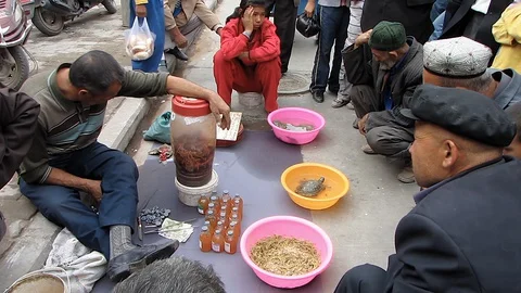 Uyghur men facing a sitting man with bowl of scorpions  Vidéo 129330004