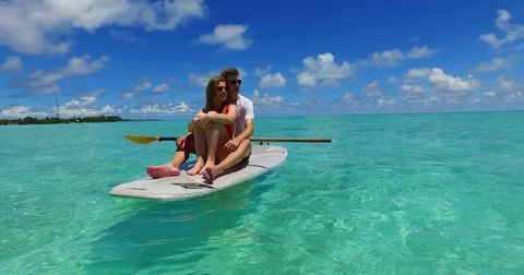 V07305 Maldives white sandy beach 2 people young couple man woman paddleboard Stock Footage