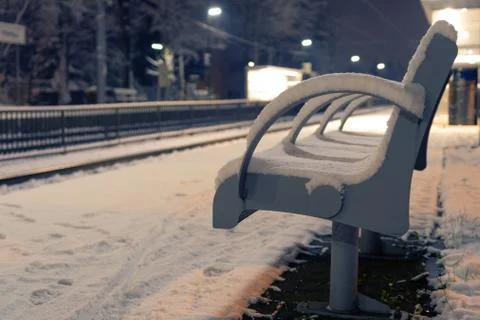 Vacant bench covered with snow at an empty train station at night Stock Photos