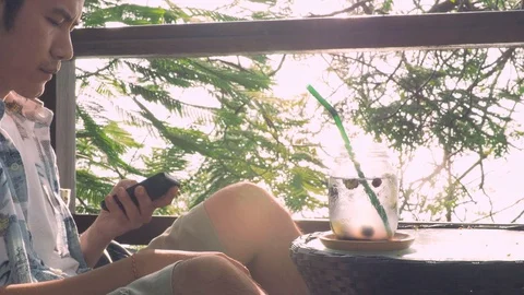 In vacation of a man sit use smartphone and drink fruit beverage under tree. Stock Footage 108842511