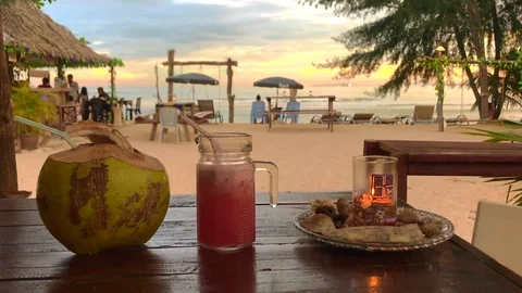 Vacation setting with a tropical coconut and fruit juice on the table and a beau Stock-Footage 101471258