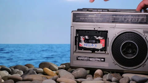 Vacationer put on stone beach old vintage retro radio tape recorder and puts on Video stock 160376603