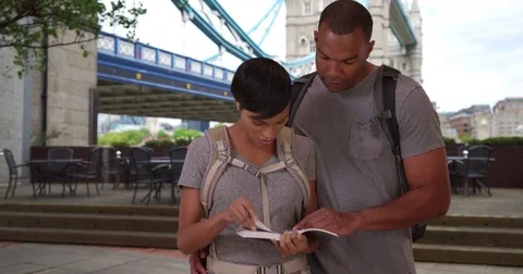 Vacationing black couple looking at guide book  for places to visit in London Видео 84188713