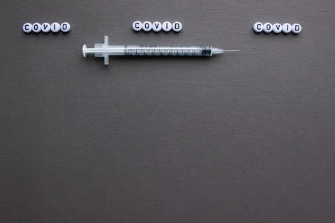 Vaccine against covid-19 and a syringe with a needle. Grey background. Stock Photos