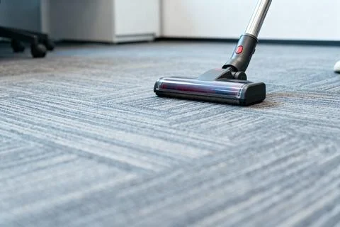 Vacuum cleaner cleaning a patterned office carpet, close-up shot Stock Photos