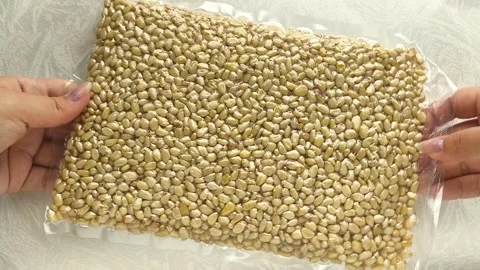 Vacuum packaging of shelled cedar pine nuts in a womans hand close-up, top view Stock Footage 316038612