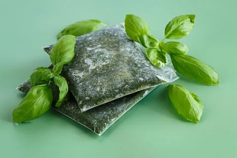 Vacuum packed frozen basil surrounded by fresh leaves on green background Stock Photos