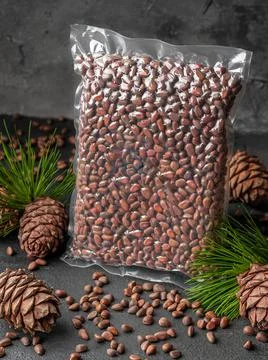 Vacuum packed pine nuts in shell. Nearby are pine cones, nuts and needles. Da Stock Photos