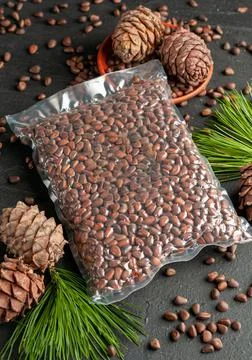 Vacuum packed pine nuts in shell. Nearby are pine cones, nuts and needles. Da Stock Photos