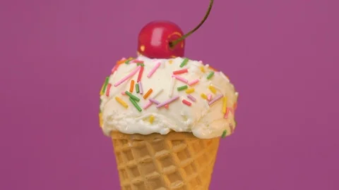 Vaffle cone of vanilla ice cream with sprinkles and cherry on pink background Stock Footage 108728370