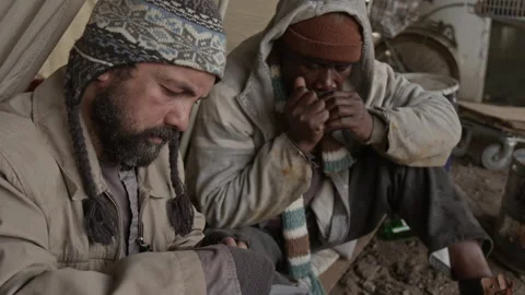 Vagabond Sewing up Hole in Pants while Sitting next to Hobo Playing Harmonica Vidéo 317310817