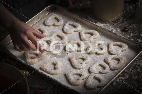 Valentine's Day baking, woman arranging heart shaped biscuits on a baking tra Stock Photos