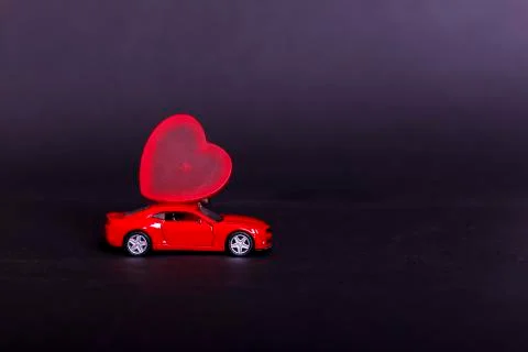Valentine's day on dark background with miniature red toy car carrying a hear Foto stock