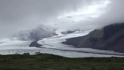Valley glacier slithers down between mountain sides with heavy dark clouds 2 Stock Footage 136616086