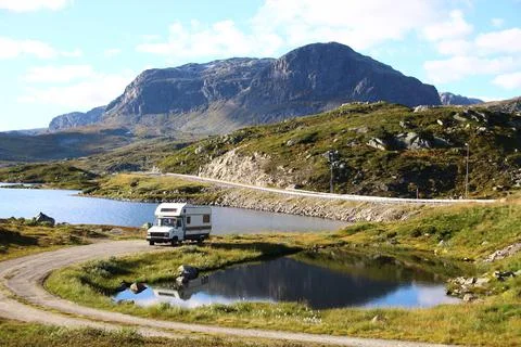 Van parked between mountains and lake with cloudy sky Stock Photos