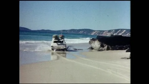 Van with surfboards goes through shorebreak an around rocks. Video stock 149447855