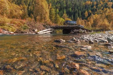 Van SUV with a trailer on a log bridge through the forest river Stock Photos